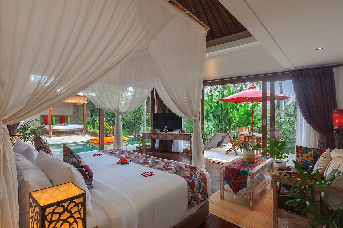 A spacious bedroom with a large bed, a TV, and a view of a pool and garden.