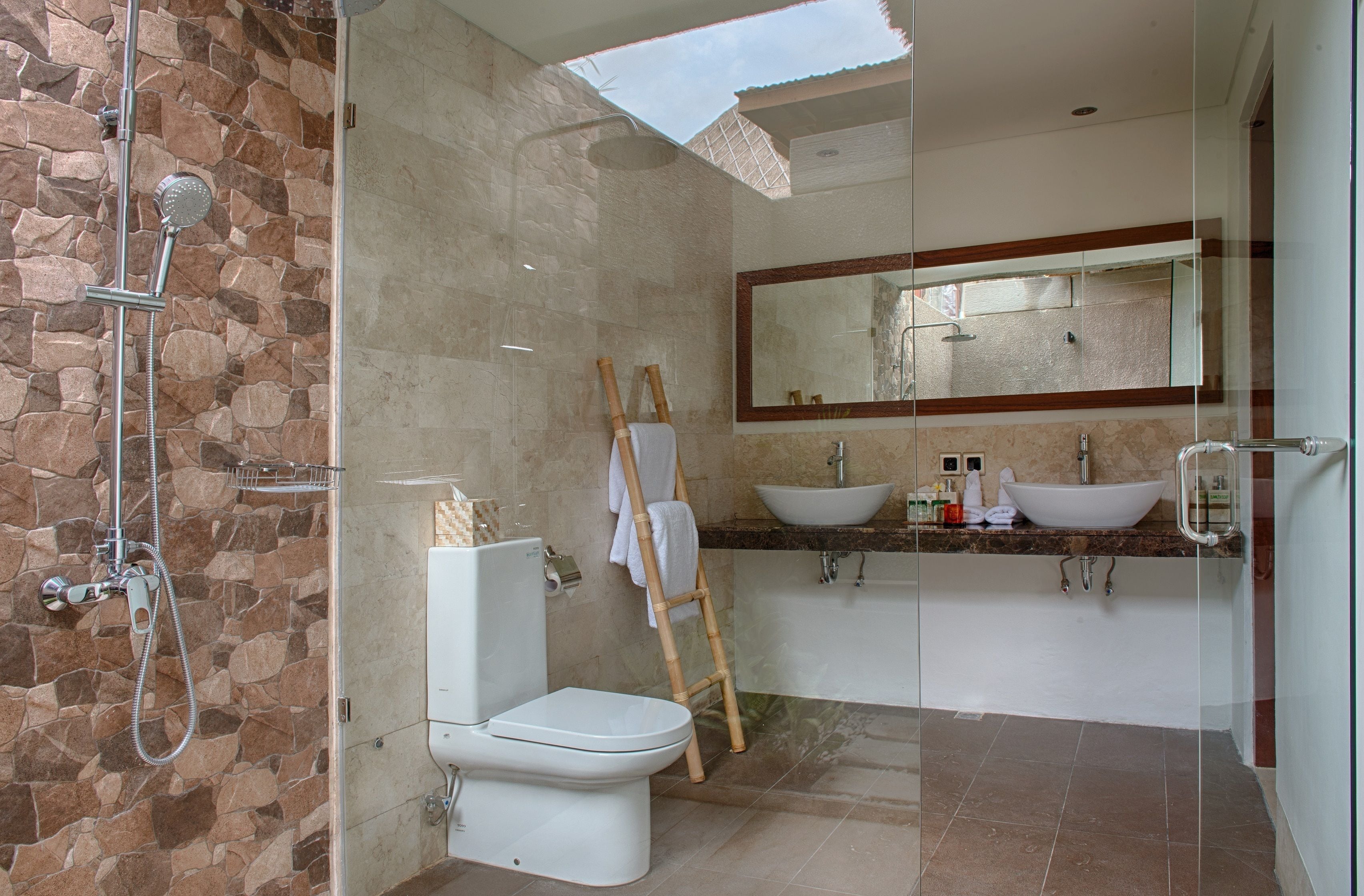 Un baño moderno con pared de piedra, cabina de ducha de vidrio, inodoro, lavabo y un espejo grande.