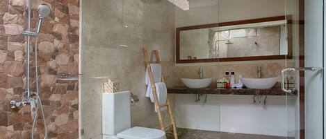 Un baño moderno con pared de piedra, cabina de ducha de vidrio, inodoro, lavabo y un espejo grande.