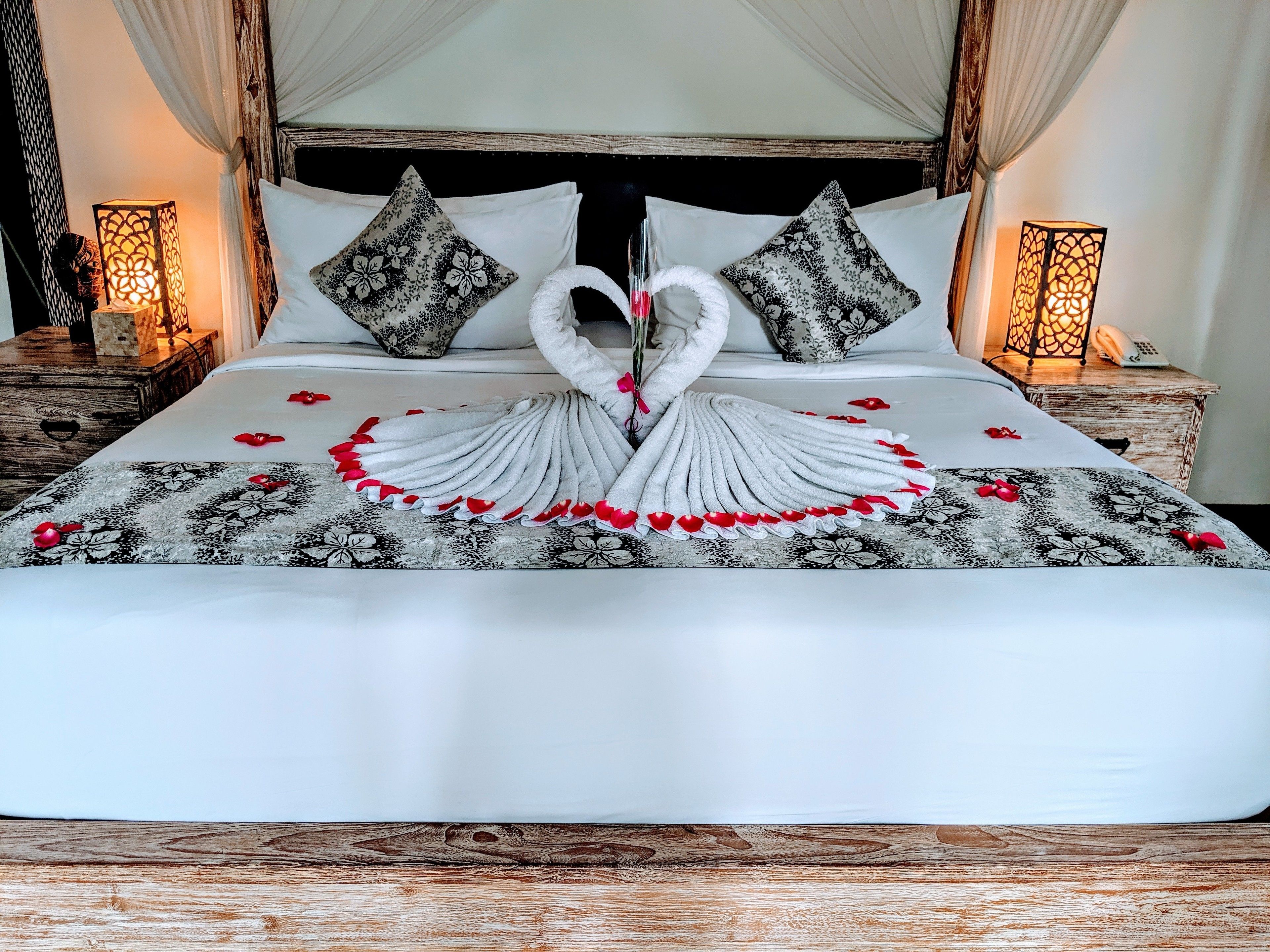 Una cama con una toalla dispuesta en forma de corazón y pétalos de rosa.