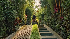 Un sentier bordé d’une végétation luxuriante et agrémenté d’un cheminement décoratif qui mène à une construction située au bout.