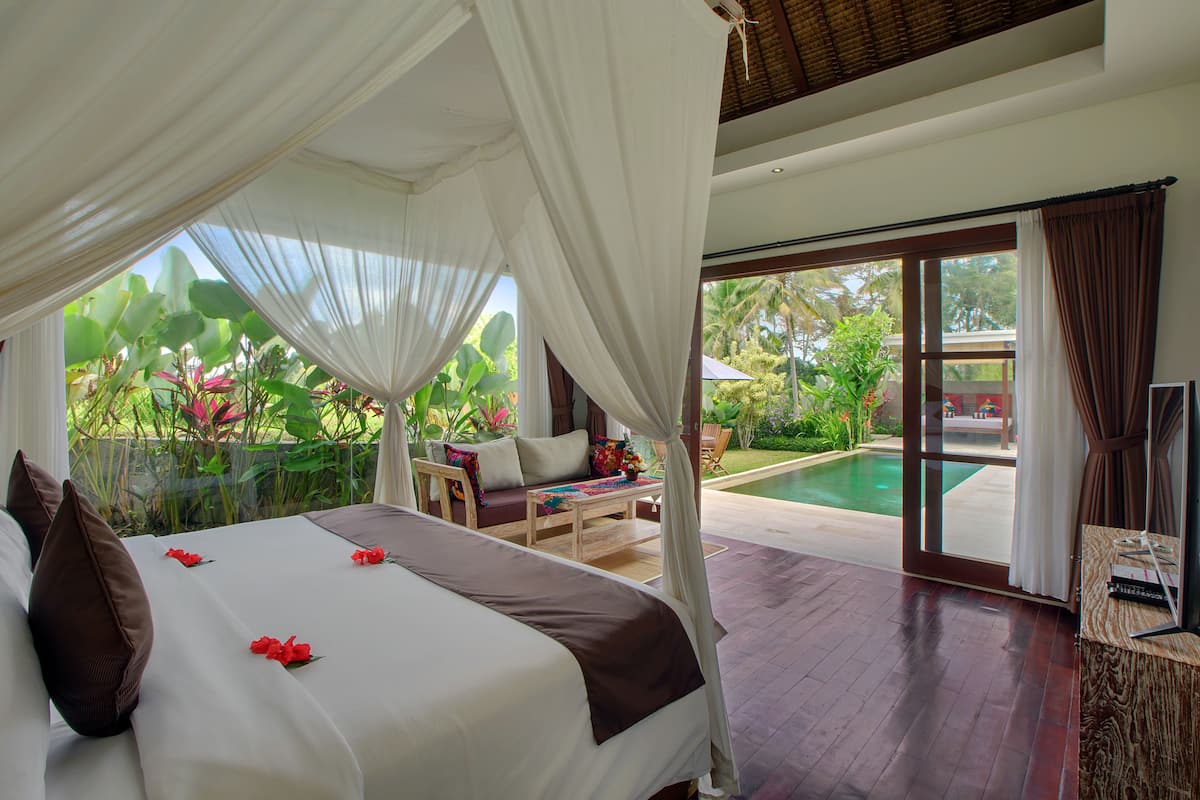A bedroom with a bed, a view of a swimming pool, and a balcony with outdoor furniture.