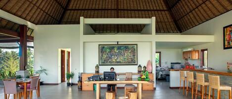 A spacious indoor area with a high ceiling, a dining table with chairs, a bar area with stools, and a kitchen in the background.