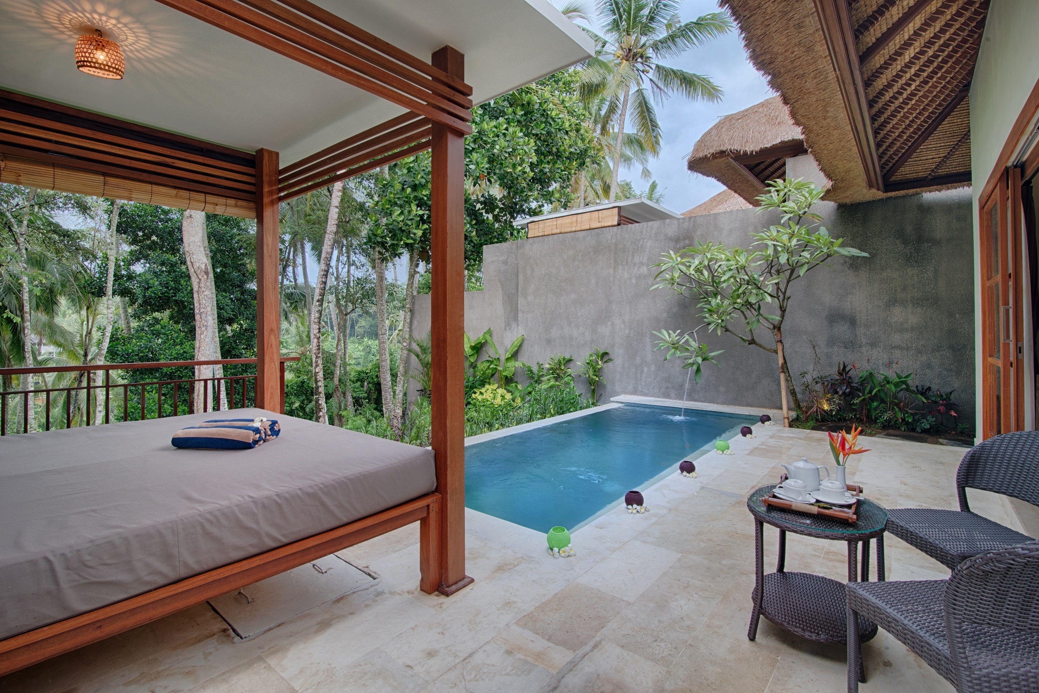 A bedroom with a bed, a small table with a vase, and a pool in the background.