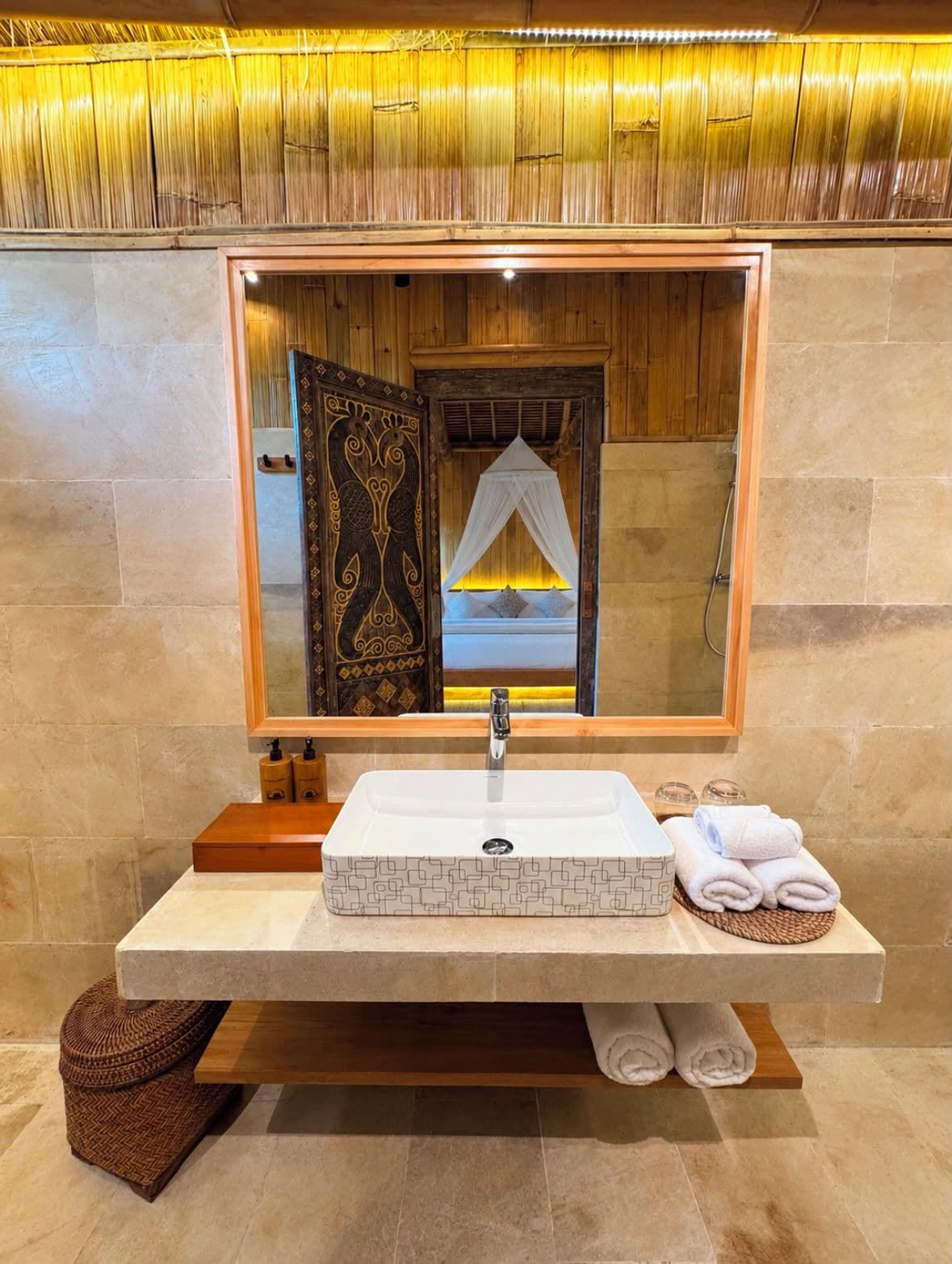 A bathroom with a large mirror, a white sink, and a wooden vanity.