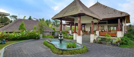 A resort with thatched-roof structures, a central fountain, and a paved walkway.