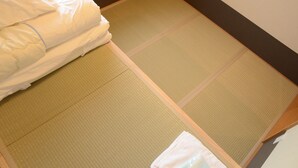 Quarto com esteiras de tatame, cama com roupa de cama branca e uma pequena lixeira branca.