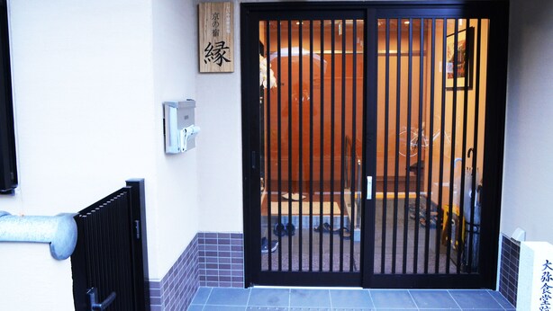 Entrada de hotel com portão preto, uma placa com caracteres japoneses e piso de azulejos.