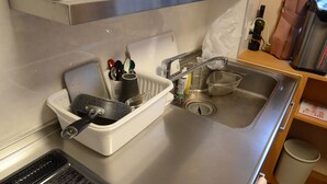 Uma cozinha com pia, escorredor de louça, garrafa de detergente e lixeira.