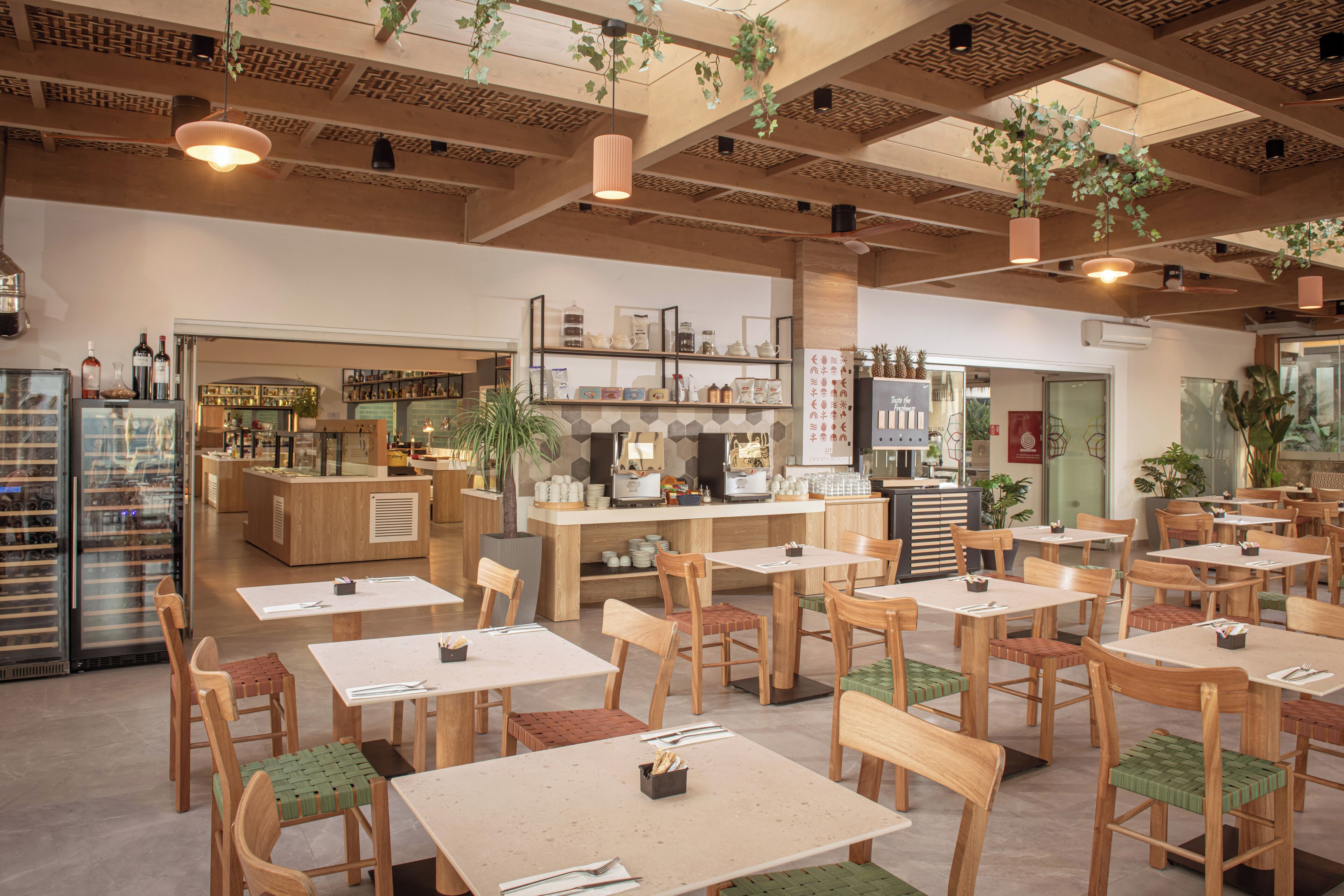 Een café met houten tafels en stoelen, een toonbank met verschillende producten en hangende planten.