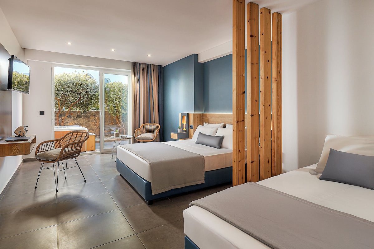 Ein modernes Hotelzimmer mit einem großen Bett, einem Einzelbett, einem Schreibtisch und einem Stuhl. Es gibt ein Fenster mit Vorhängen, einen Fernseher und eine Holzwand.