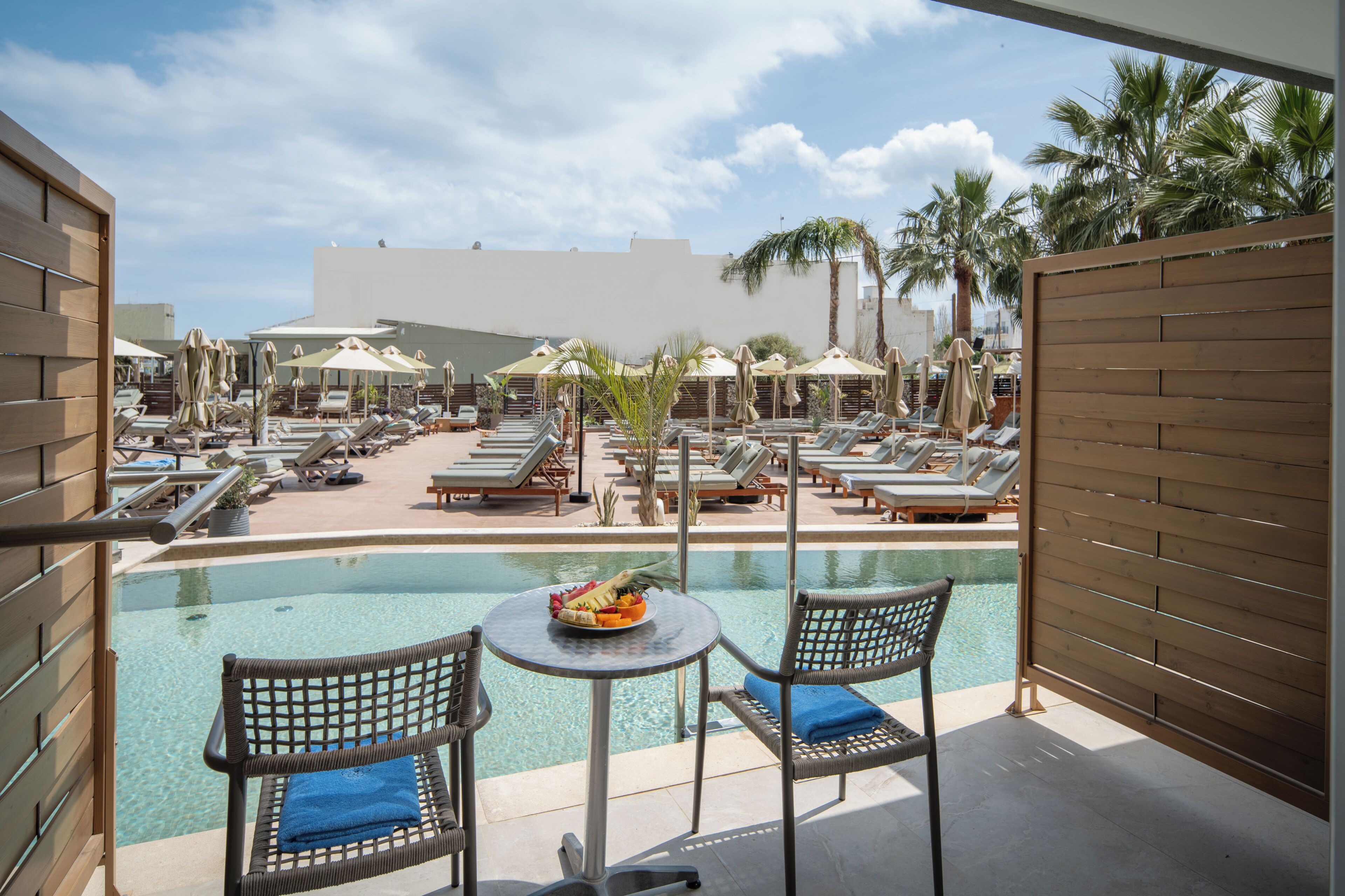 A poolside area with lounge chairs, umbrellas, and a table with a fruit bowl.
