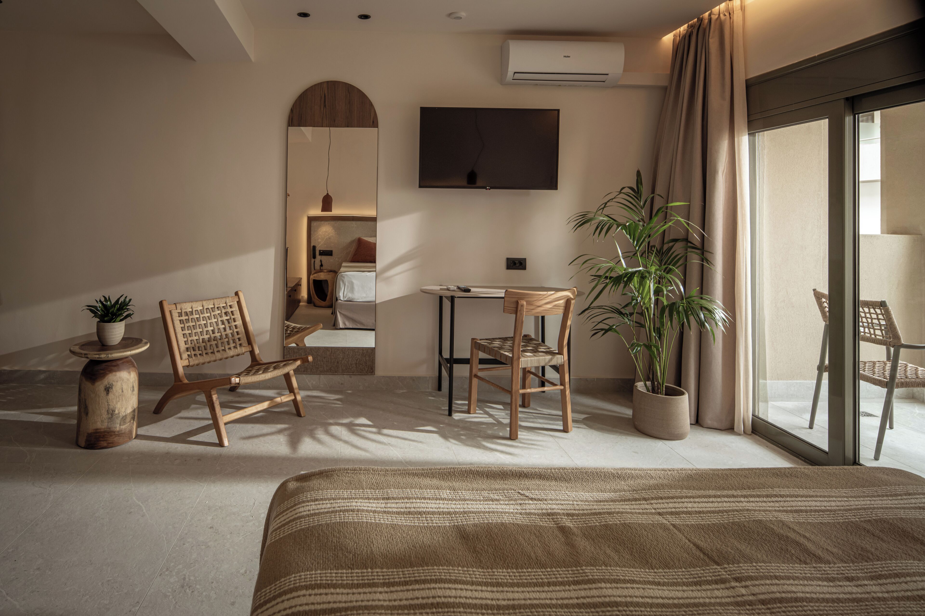 Una habitación de hotel moderna con una cama grande, un escritorio, dos sillas, una planta en maceta y un televisor.