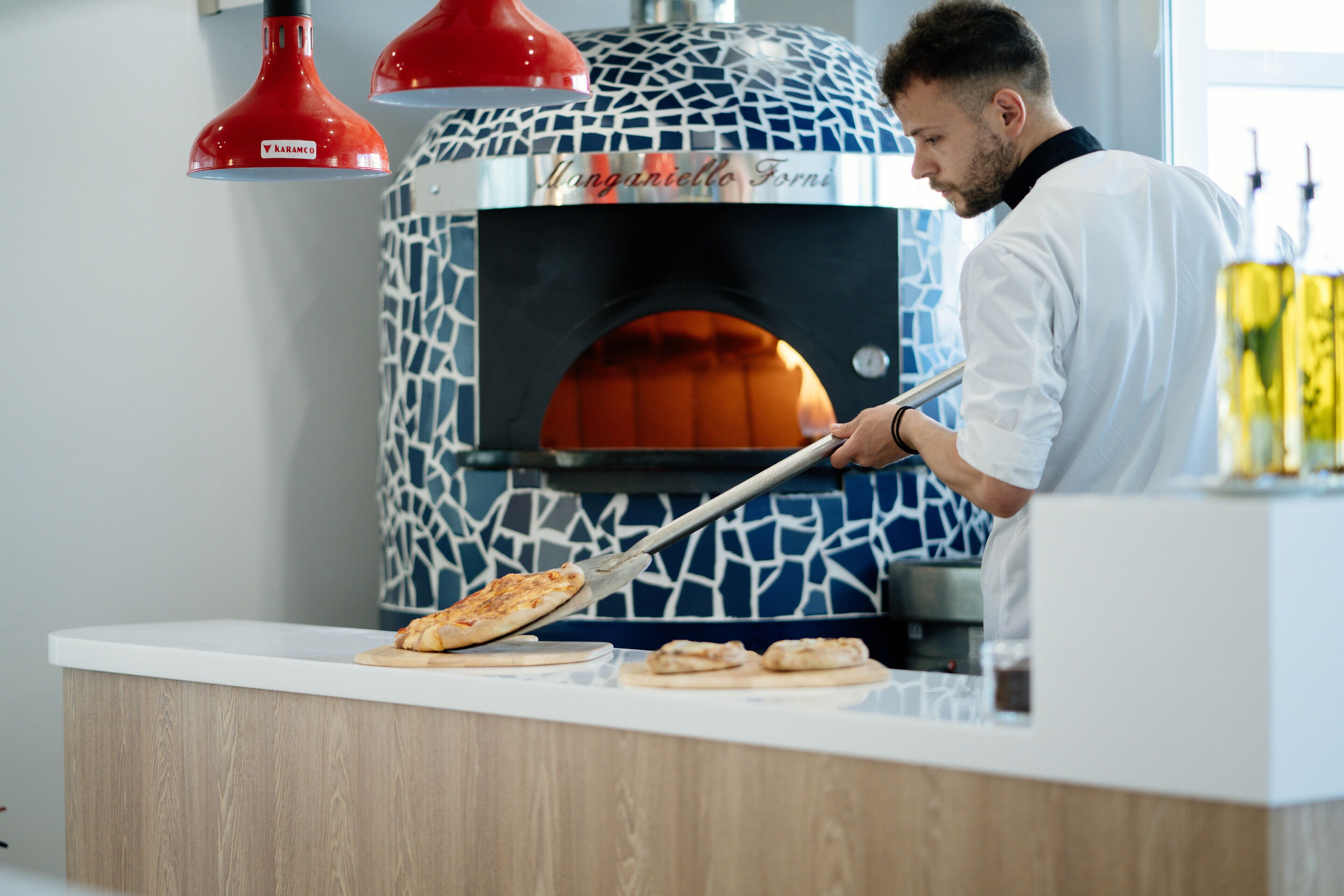 Una persona usando un horno de pizza con un diseño estampado, una encimera blanca y una lámpara roja colgante.