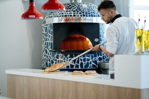 Una persona usando un horno de pizza con un diseño estampado, una encimera blanca y una lámpara roja colgante.