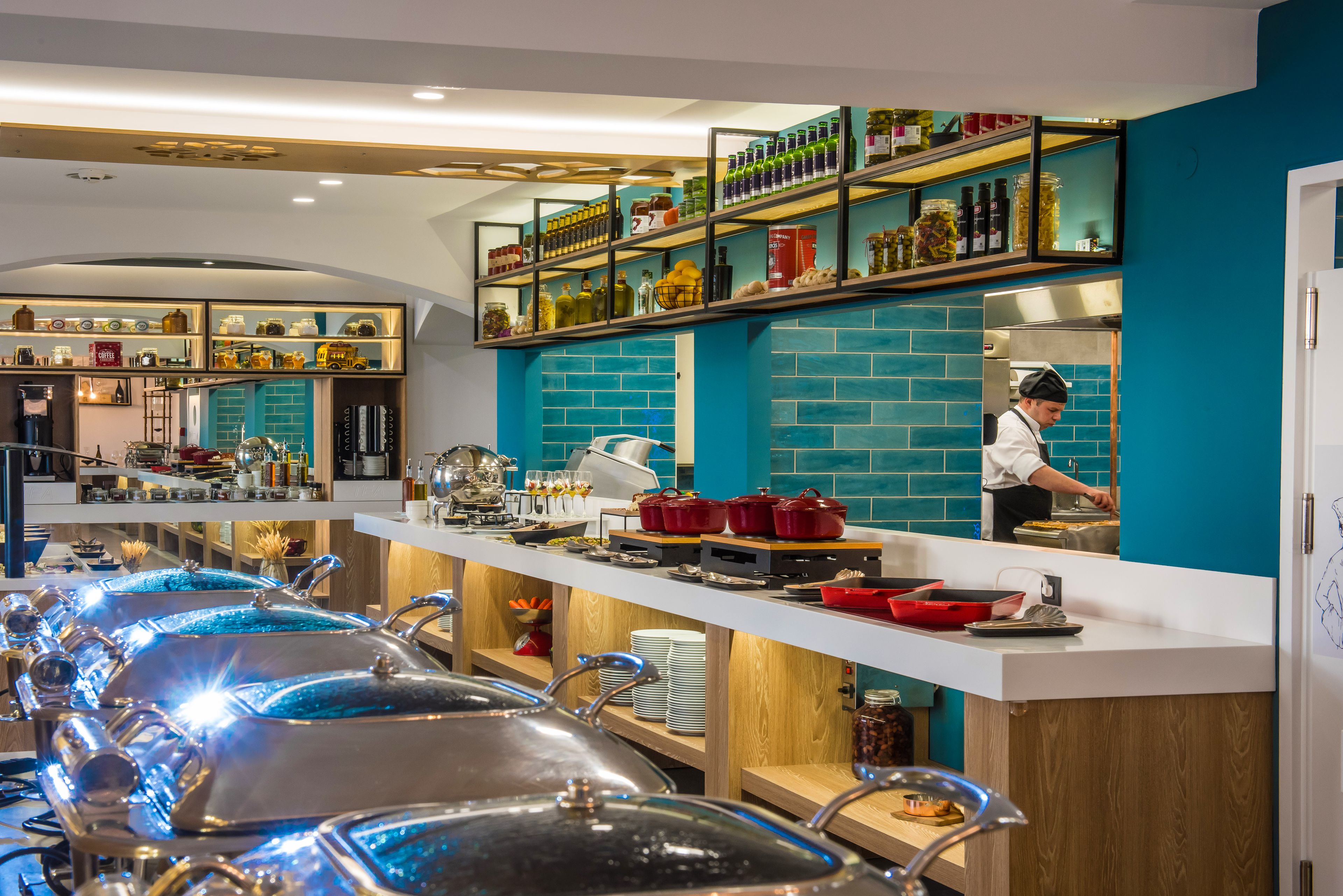 A buffet setup with multiple serving stations, a chef preparing food, and a variety of food items and condiments on shelves.
