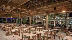 Een eetruimte binnenshuis met meerdere tafels en stoelen, plafondventilatoren en hangende planten.