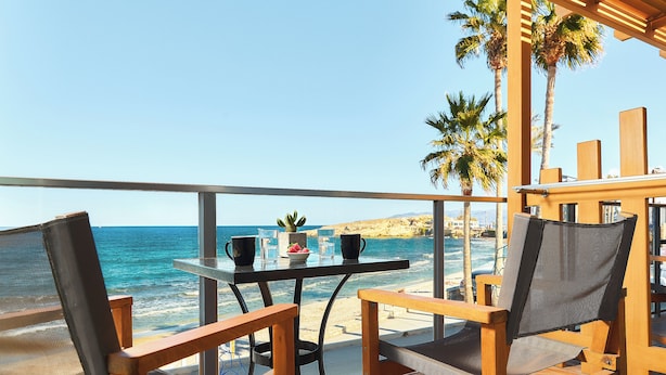 Een balkon met een tafel, stoelen en uitzicht op zee.