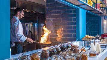 A chef cooking in a kitchen with a brick wall and a buffet with various food items.