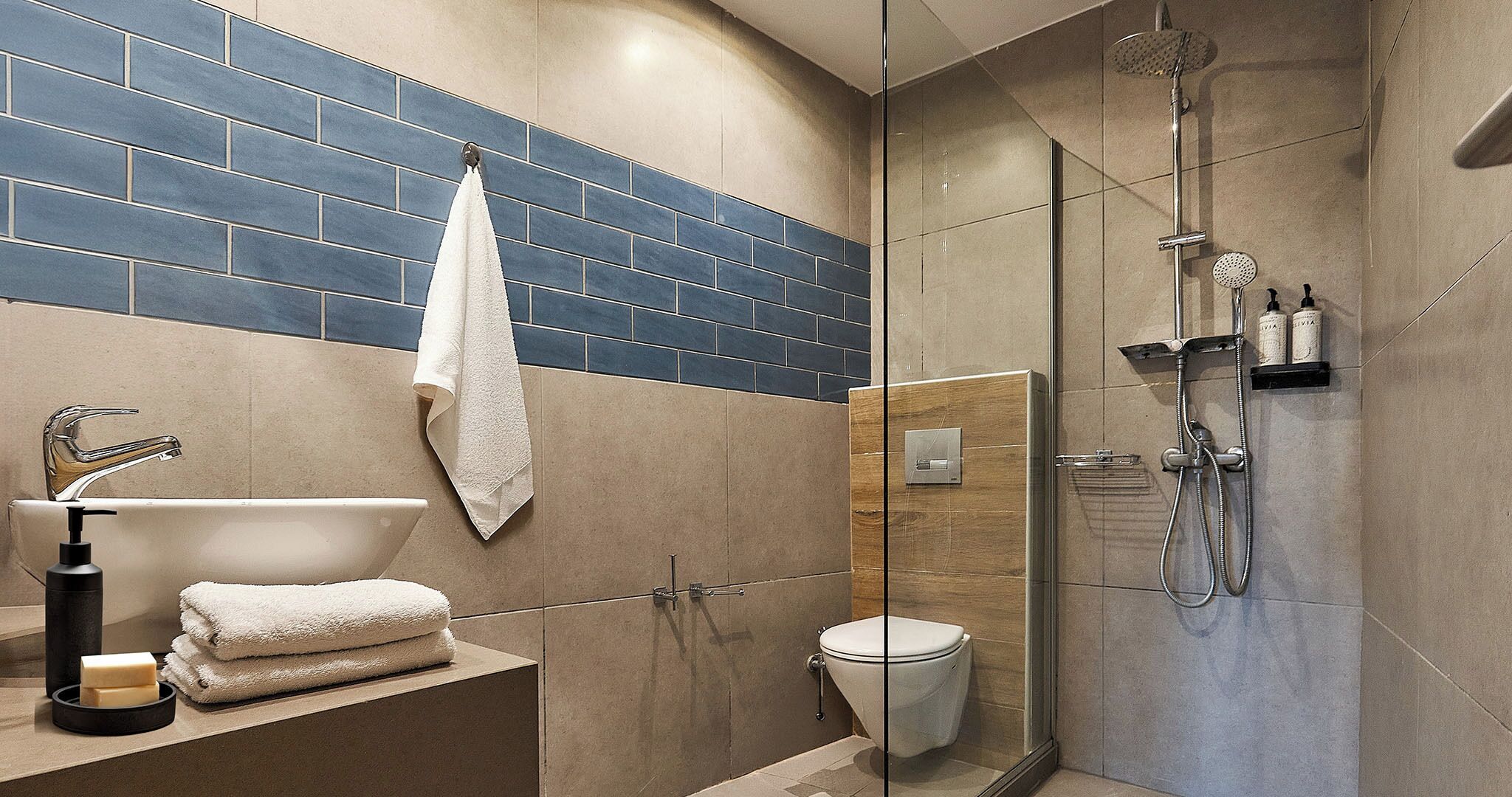 Un baño moderno con ducha de vidrio, lavamanos blanco y pared con azulejos color beige.