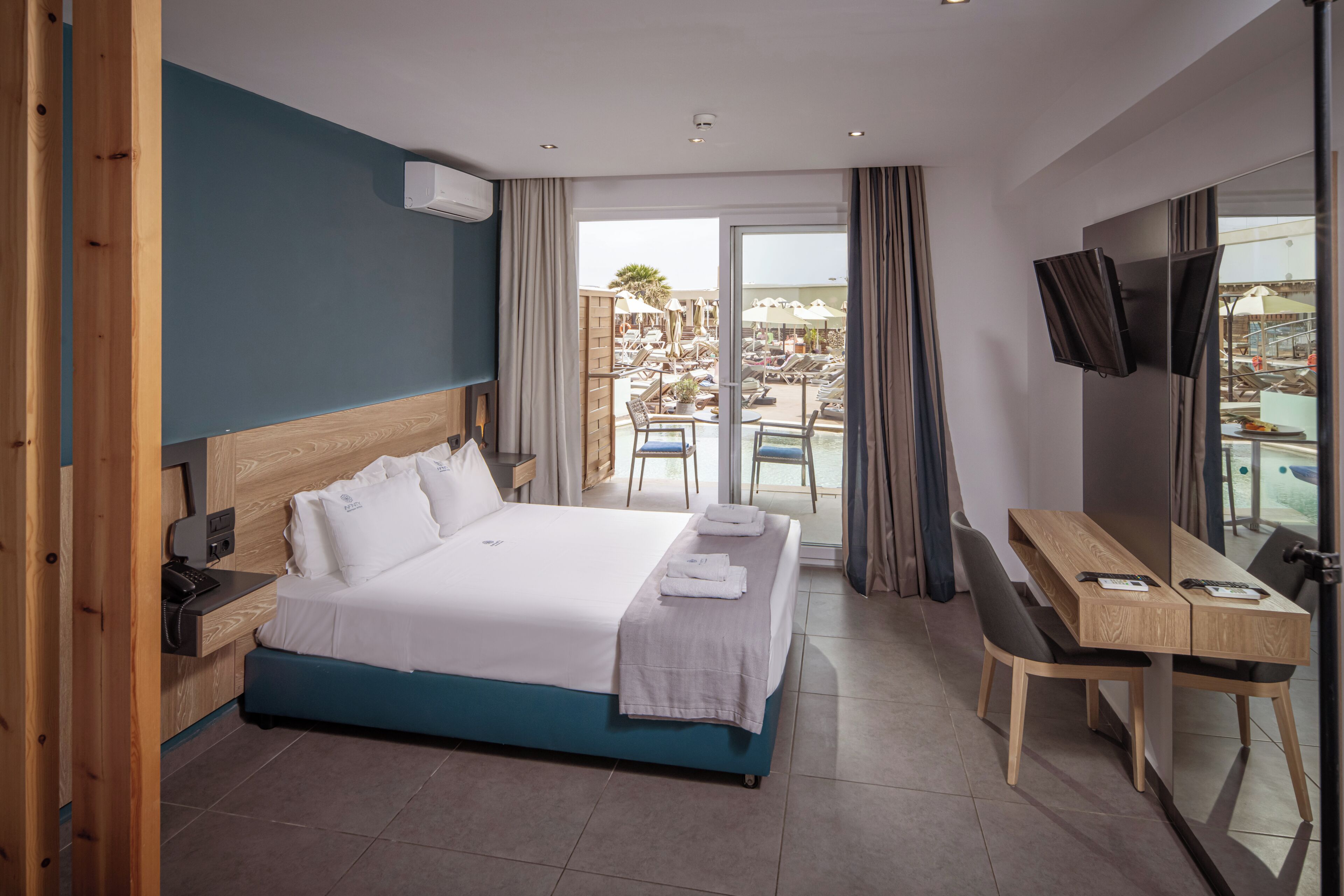 Habitación de hotel con cama, escritorio, televisor y balcón con mobiliario de exterior.