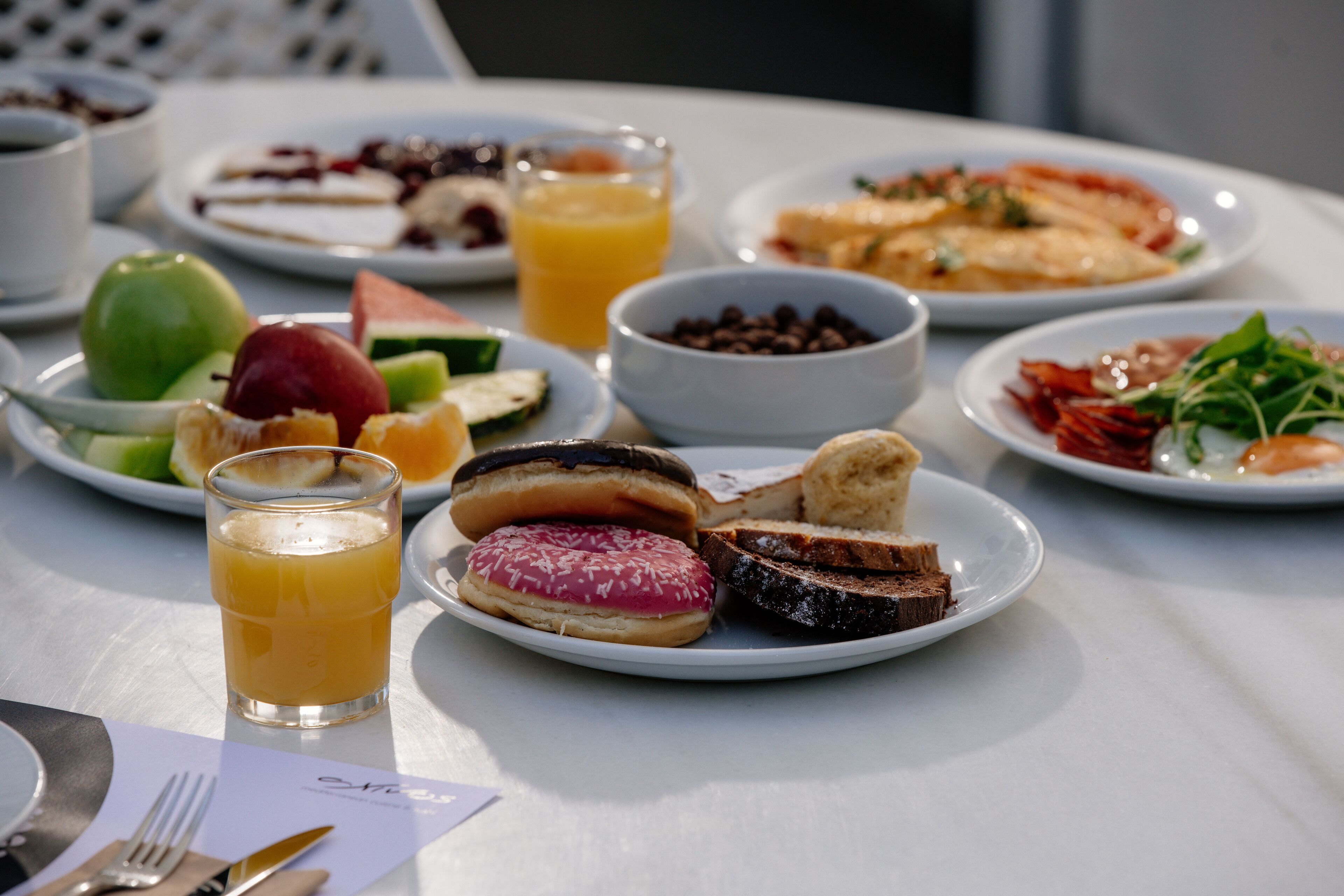 A table with various breakfast items including fruits, pastries, and a glass of orange juice.