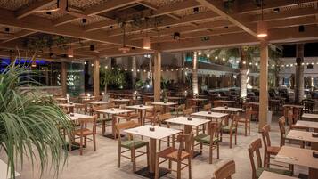 A spacious indoor dining area with multiple tables and chairs, large windows, and hanging plants.