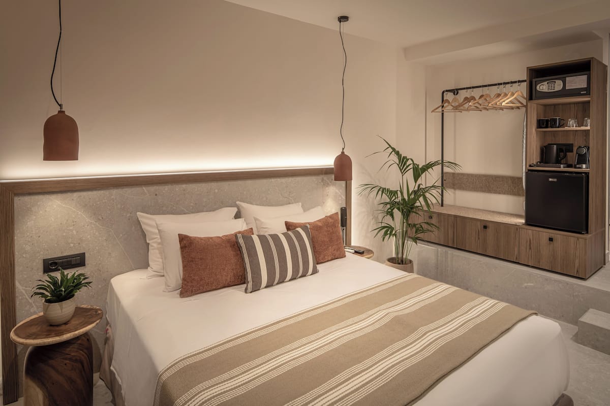 Ein modernes Hotelzimmer mit einem großen Bett, Nachttischen, einer Pflanze und einer eingebauten TV-Konsole.