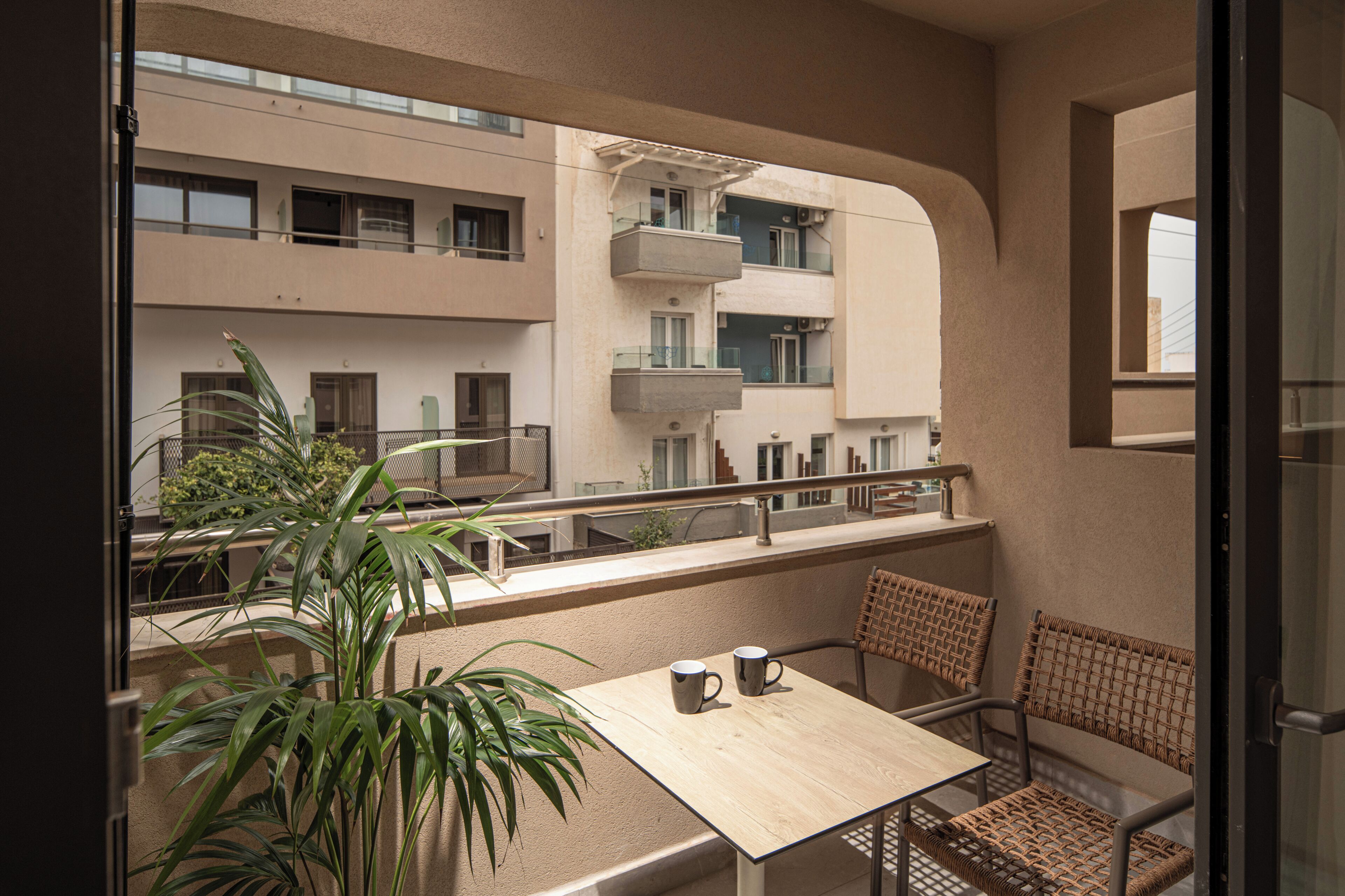 Un balcó amb taula i cadires, una planta en test i vista d'un edifici d'àmbit urbà.
