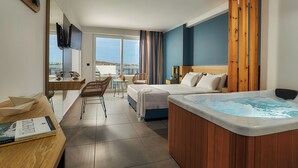 Een moderne hotelkamer met een groot bed, een houten hoofdeinde, een whirlpool, een bureau met een stoel en uitzicht op zee.