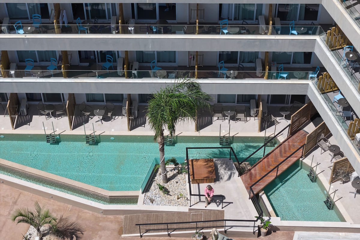 Ein mehrgeschossiges Hotel mit Außenpools, Sitzbereichen und einer Palme.