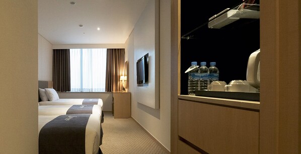 A hotel room with two beds, a TV, a window with curtains, a nightstand, and a minibar with bottled water. - Hotel Venue G (Seoul)