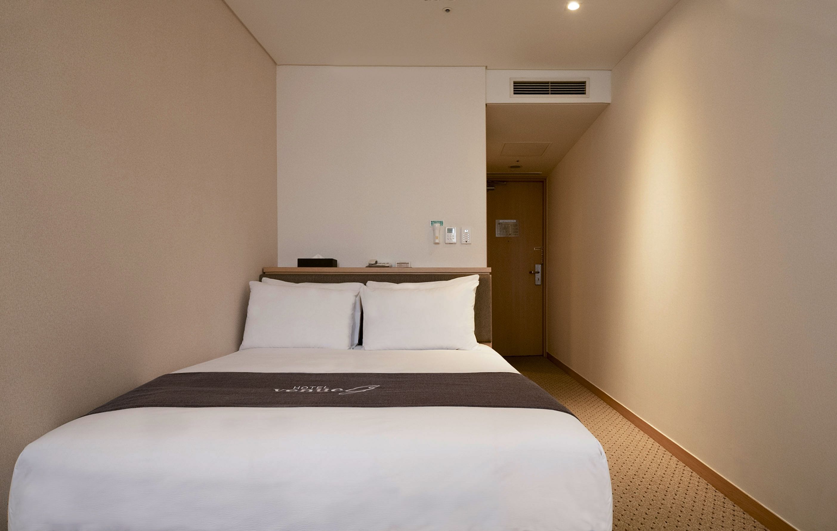 A hotel room with a bed, a bedside table, a nightstand, and a door leading to another room.
