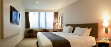 Ein Hotelzimmer mit einem großen Bett, einem Schreibtisch, einem Sessel, einem Fernseher und einer Lampe.