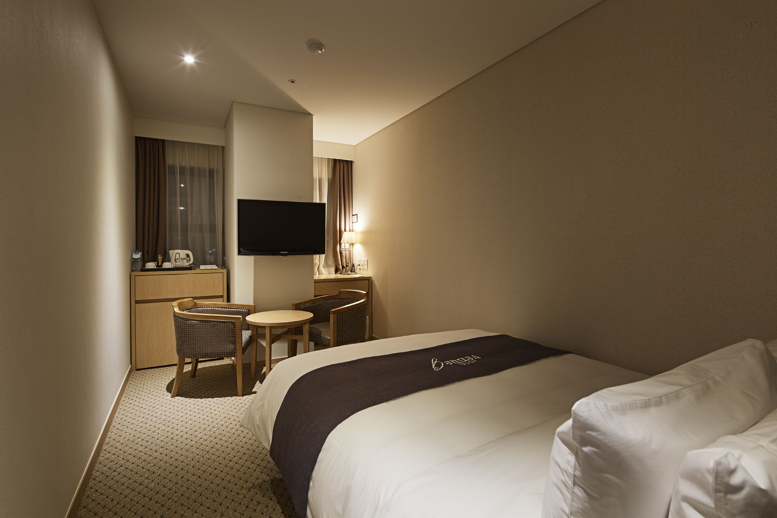 A hotel room with a large bed, a desk with a chair, a television, and a small table.