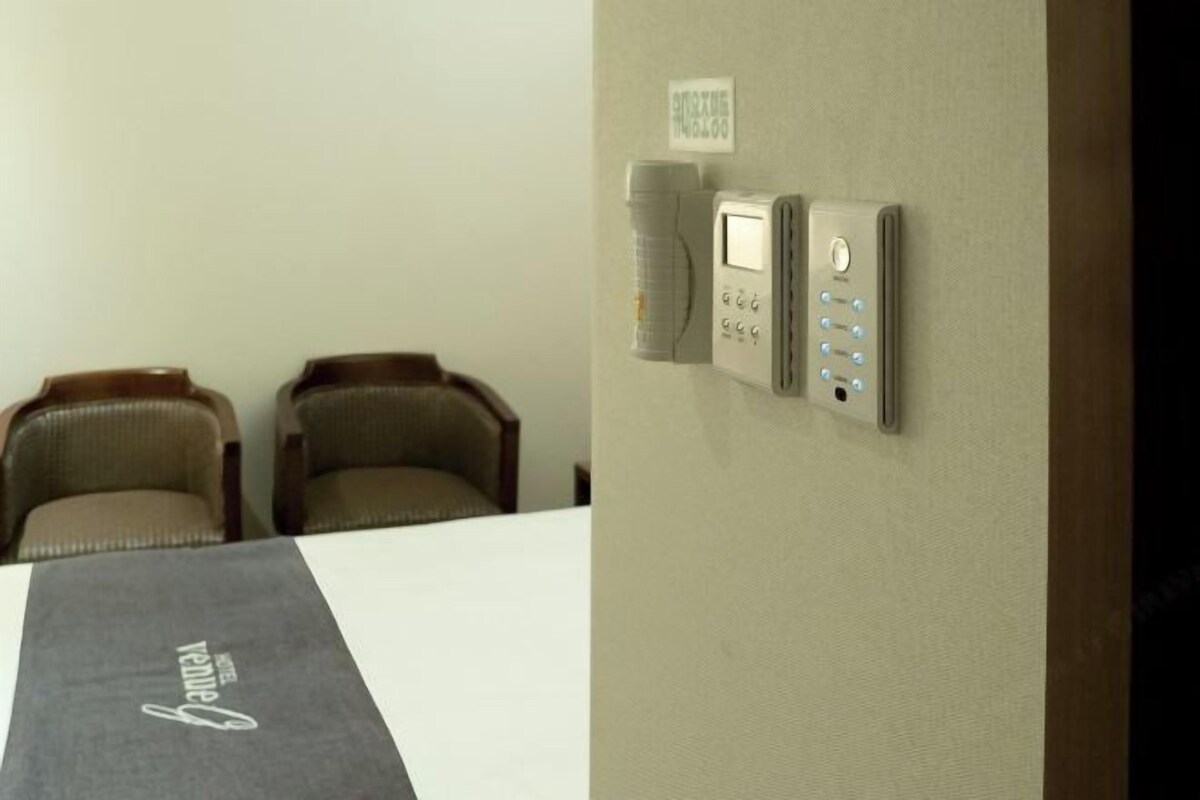 A hotel room with a bed, a bedside table, and a wall-mounted control panel.