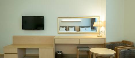 Een hotelkamer met een houten bureau, een televisie, een spiegel, een lamp en twee stoelen.