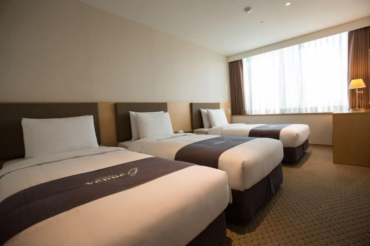 A hotel room with three beds, a desk, and a large window with curtains.