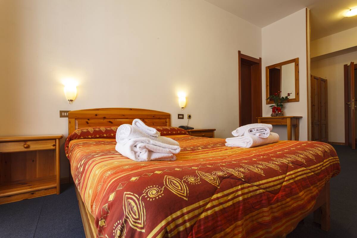 A hotel room with a large bed, two bedside tables, a nightstand, a mirror, and a door leading to another room.