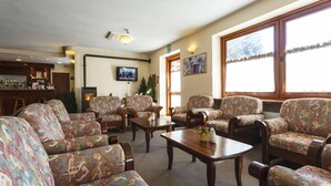 A cozy living room with patterned sofas and wooden coffee tables, a television mounted on the wall, and a large window with curtains. - Club Hotel Solaris (Cesana Torinese)