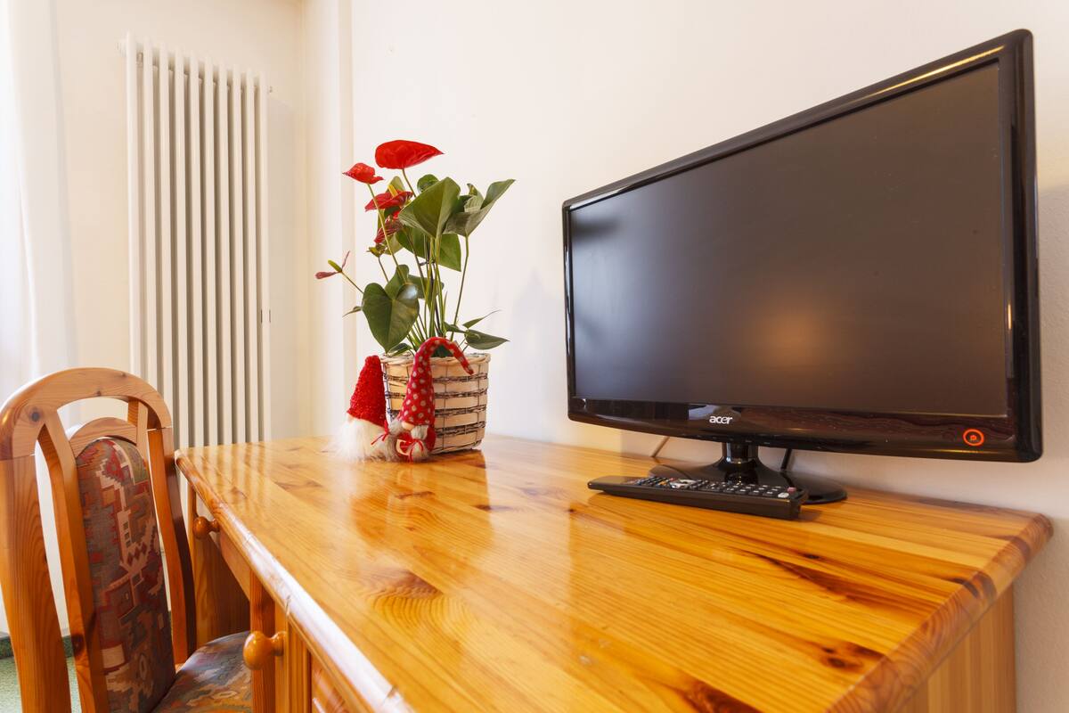 A wooden desk with a computer monitor, a chair, and a potted plant with red flowers.