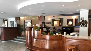 A spacious lobby with a curved wooden reception desk, a dartboard, and a bar area with stools. - Club Hotel Solaris (Cesana Torinese)