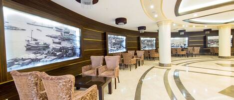 A lobby with a curved floor, large wall-mounted televisions displaying images, and a seating area with patterned chairs and tables.