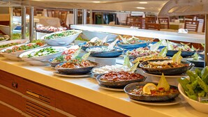 A buffet with various dishes, including salads, meats, and vegetables, arranged on a counter with a glass display case above. - Alder Resort Hotel - Ultra All Inclusive (Kemer)