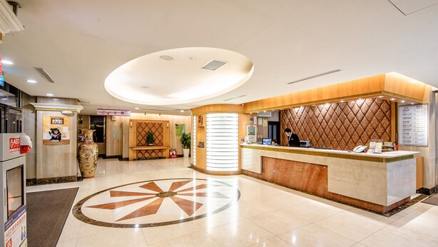 A hotel reception area with a modern design, featuring a reception desk, a large decorative vase, and a patterned floor design. - KKS Hotel (Hualien City)