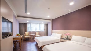 A hotel room with two beds, a desk with a chair, a small table with a vase of flowers, and a TV on the wall. - KKS Hotel (Hualien City)