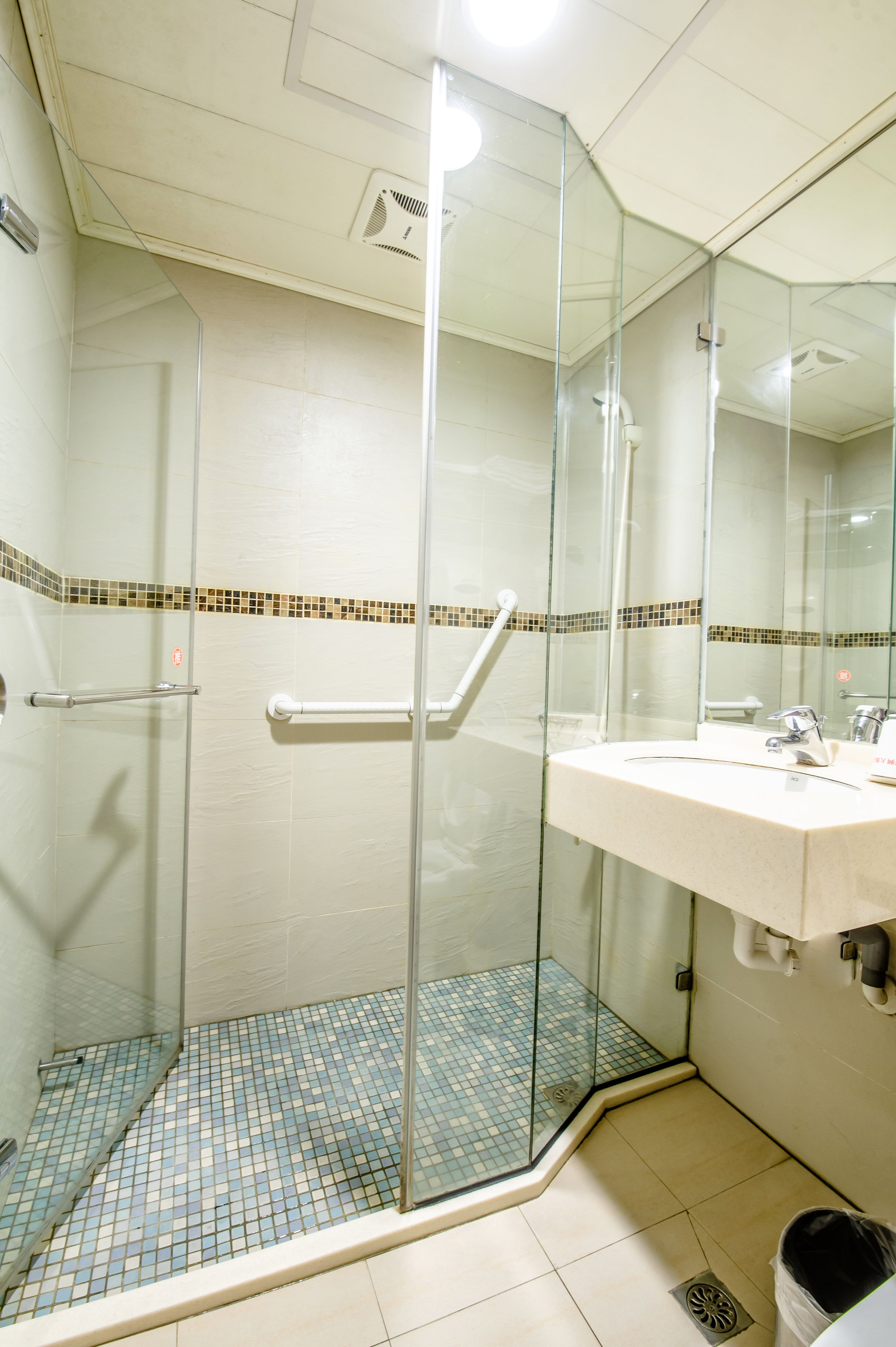 Ein Badezimmer mit einer gläsernen Duschkabine, einem weißen Waschbecken und einem Fliesenboden.