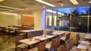 A restaurant with tables and chairs arranged in rows, large windows with a view of the outside, and a modern ceiling design. - KKS Hotel (Hualien City)