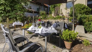 An outdoor dining area with tables set for two, surrounded by potted plants and a stone wall. - Landhotel Goldenes Kreuz (Moosbach)