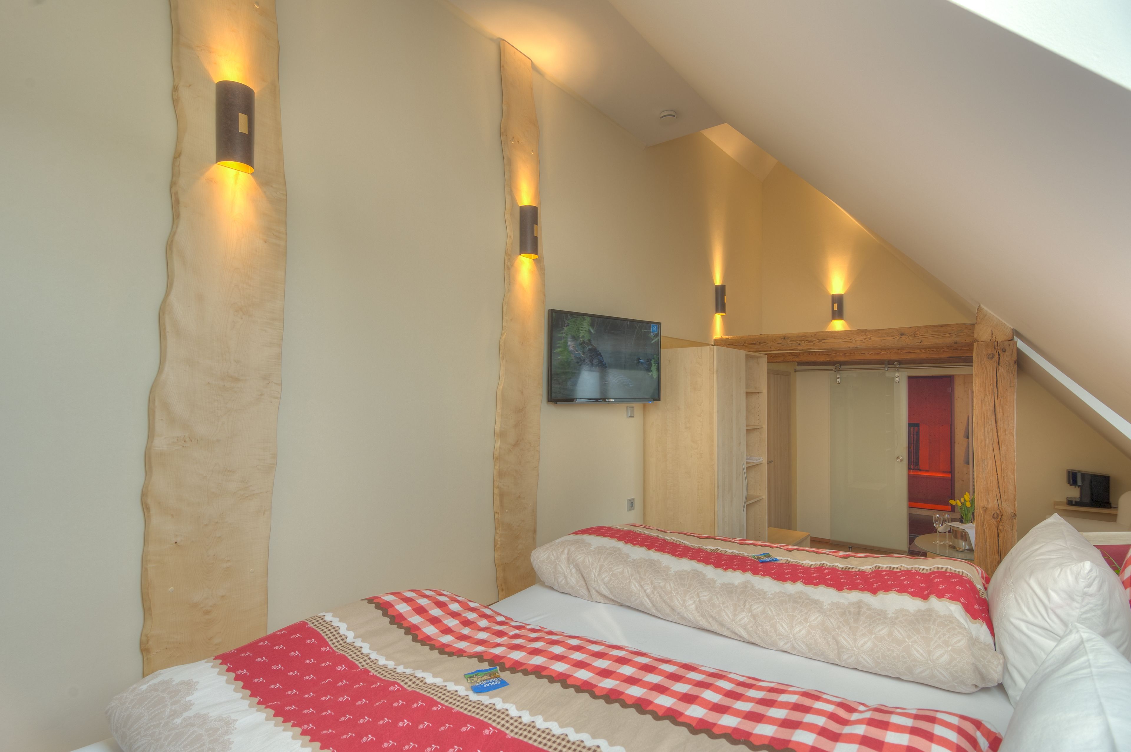 Een slaapkamer met een schuine plafond, een bed met beddengoed met een patroon, en wandlampen.